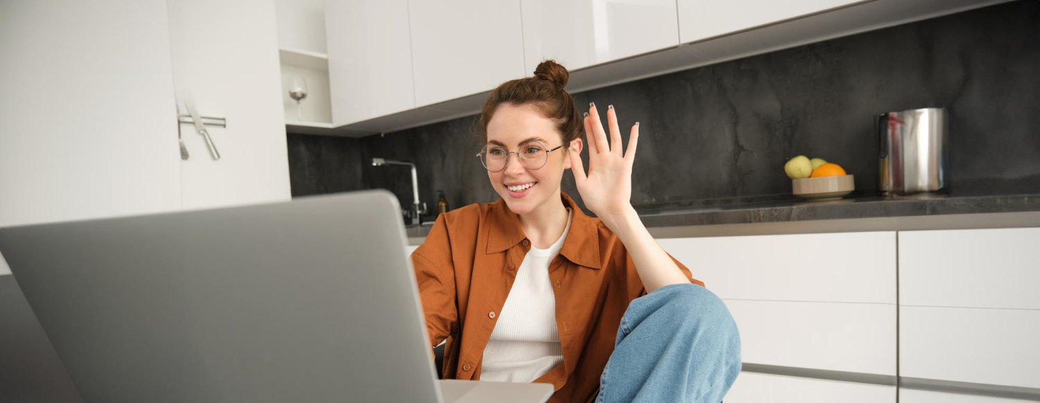 Woman waving to laptop screen on video call