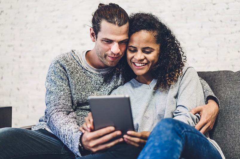 A couple sitting on a couch looking at a laptop.